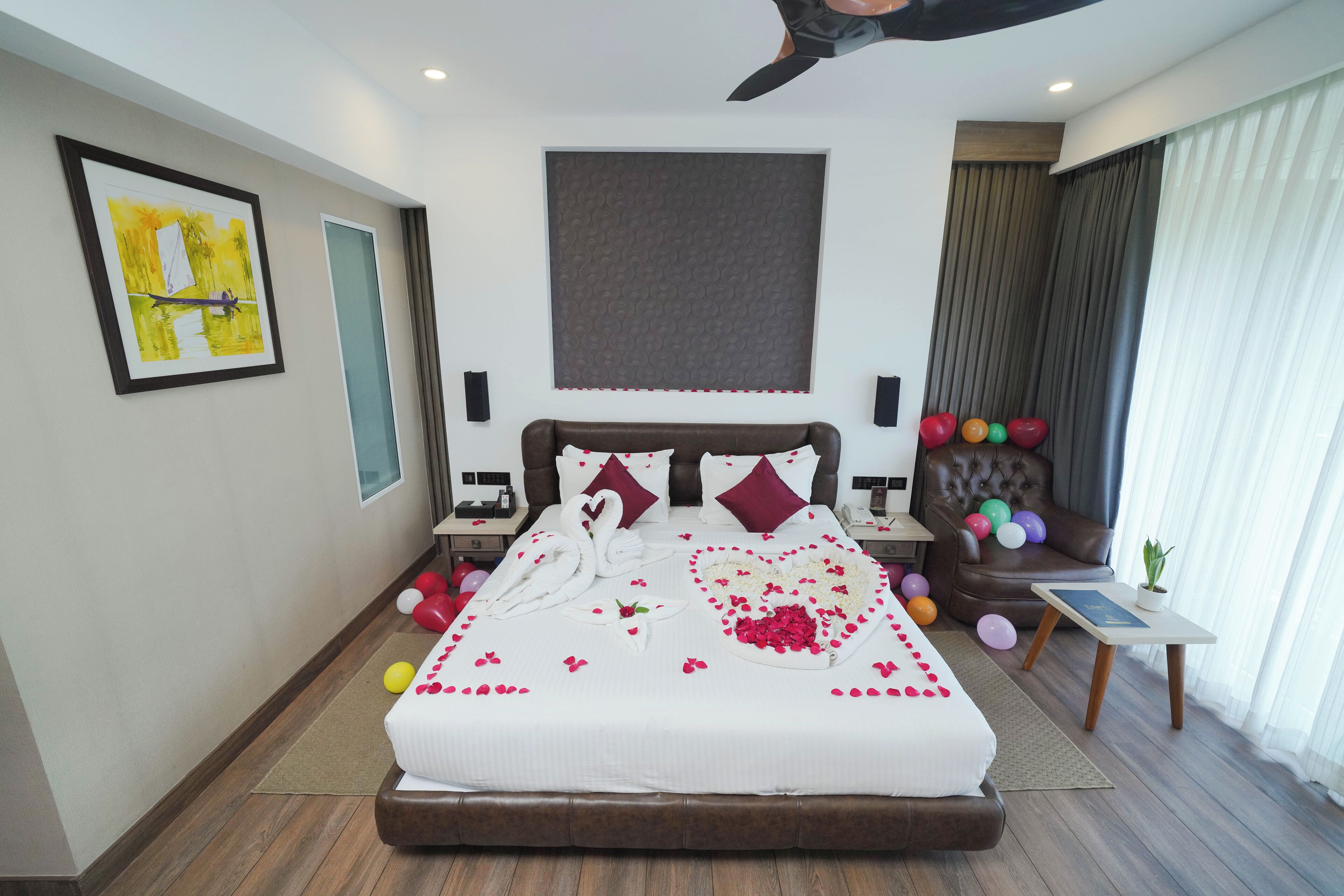 A hotel room with a large bed, a headboard, a nightstand, a chair, and a small table with a plant.