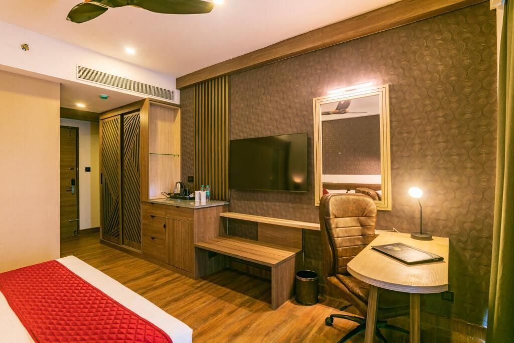 A hotel room with a bed, a desk with a chair, a television, and a mirror.