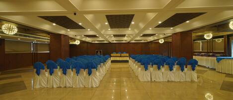 A banquet hall with rows of tables, white tablecloths, and blue chair covers.