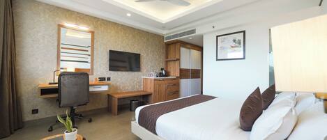 Habitación de hotel con una cama grande, un escritorio con computadora, una silla, una pequeña mesa con una planta y un ventilador de techo.