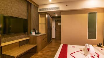 Ein Hotelzimmer mit einem großen Flachbildfernseher, Holzmöbeln, einem Bett mit roter Herzdeko und einer Minibar.