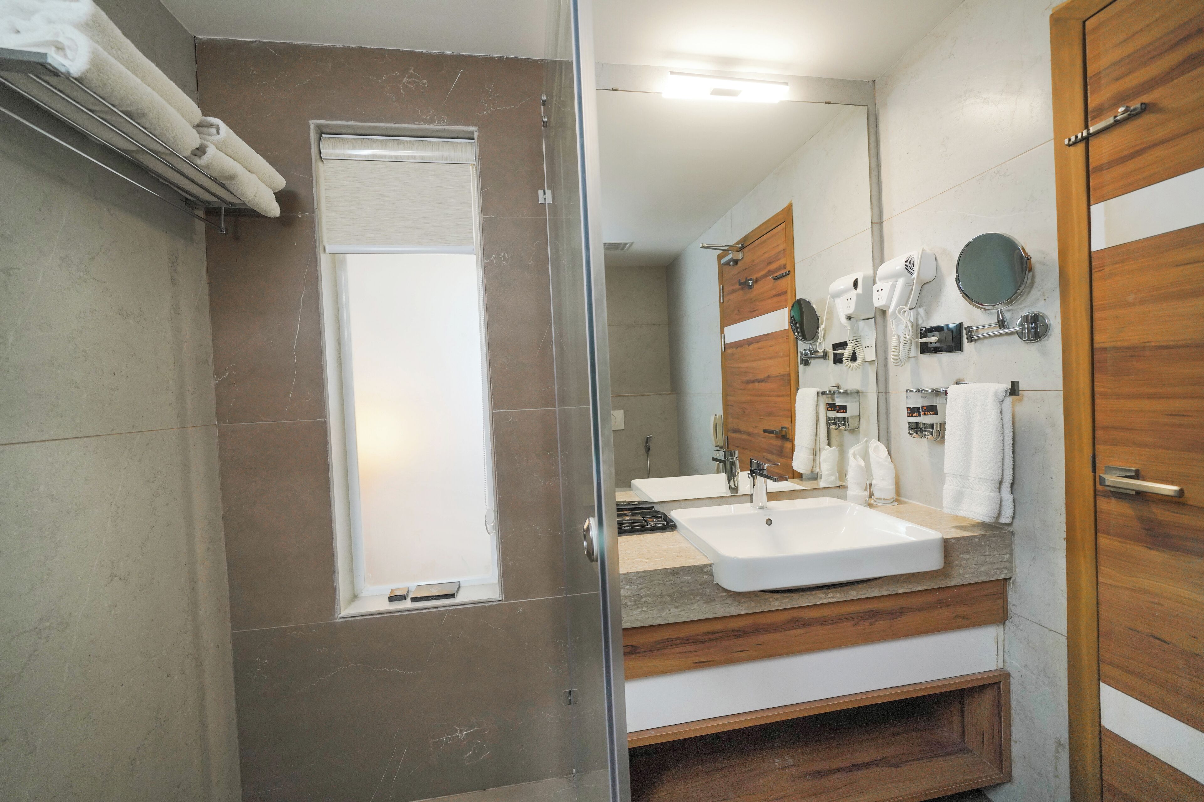 A modern bathroom with a glass shower enclosure, a vanity with a sink, and a wooden vanity with a mirror and towel rack.