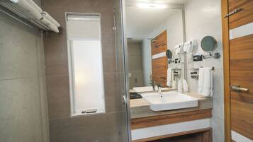 Un baño moderno con cabina de ducha de vidrio, un tocador con lavamanos y un mueble de madera con espejo y toallero.