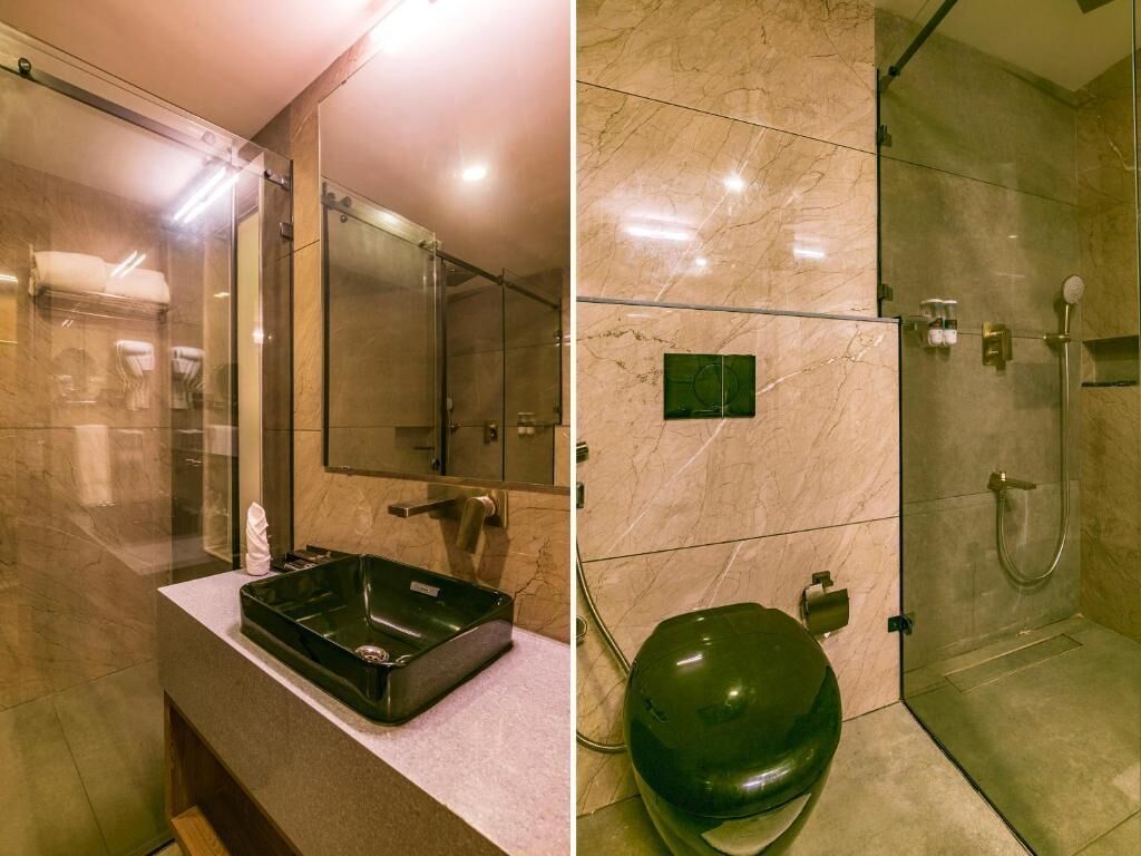A modern bathroom with a glass shower enclosure, a green toilet, and a marble-tiled wall.