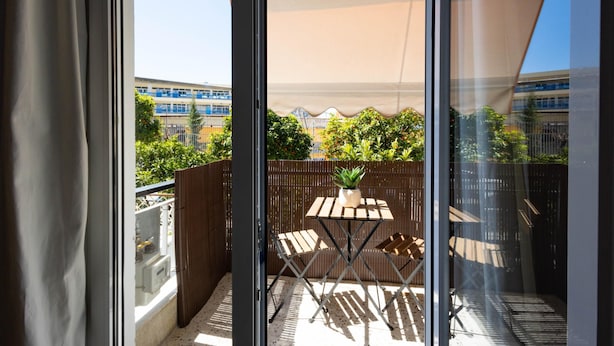 A balcony with a table and chairs, a potted plant, and a view of buildings and greenery.
