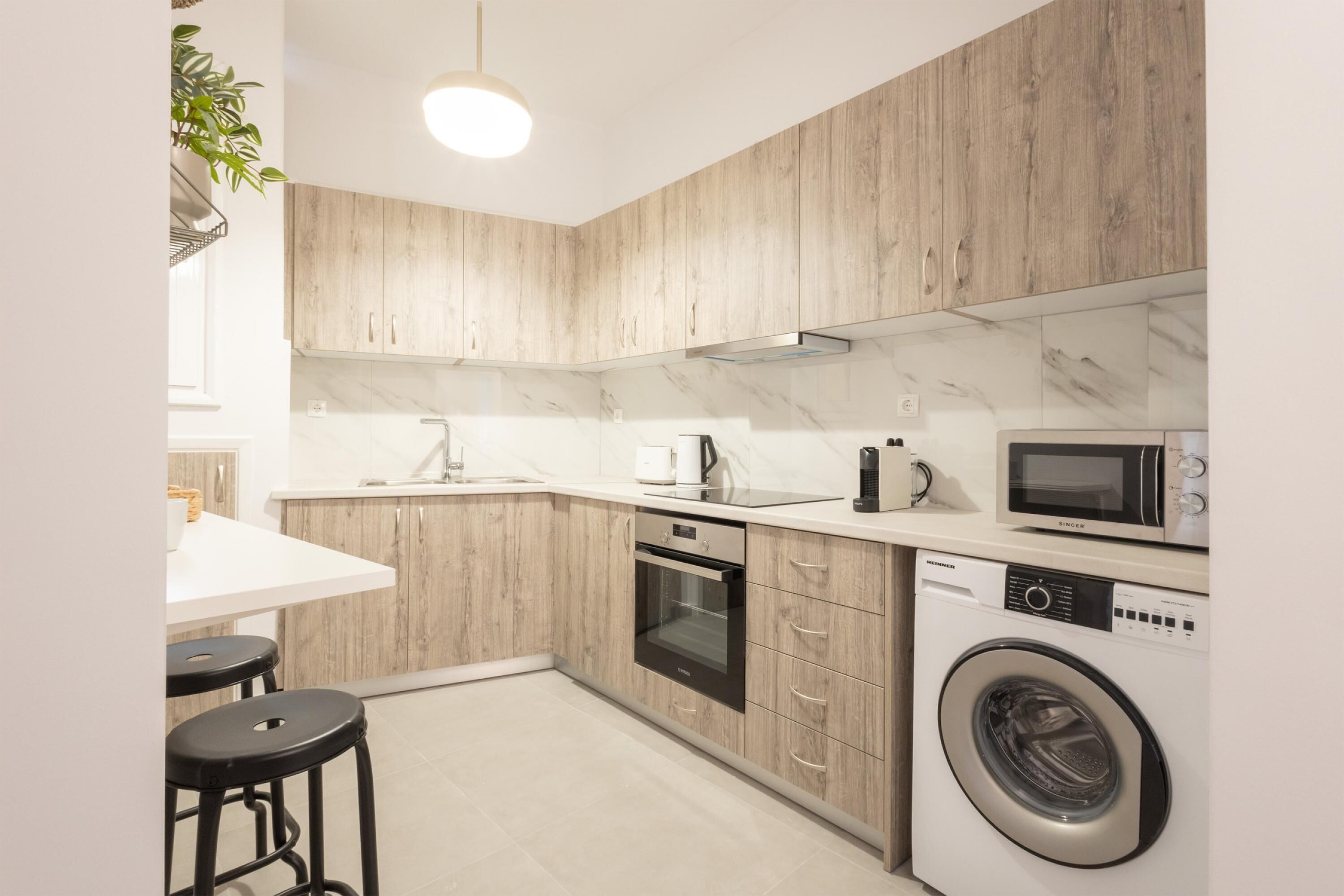 A modern kitchen with wooden cabinets, a built-in oven, a microwave, and a washing machine.