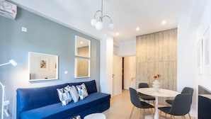 A modern living room with a blue sofa, a dining table with chairs, and a light wood accent wall.