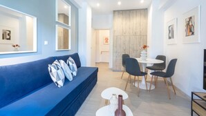 A modern living room with a blue sofa, a dining area with a white table and chairs, and artwork on the walls.