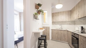 A modern kitchen with wooden cabinets, a white countertop, and a built-in oven. There are two black stools and a small white table.