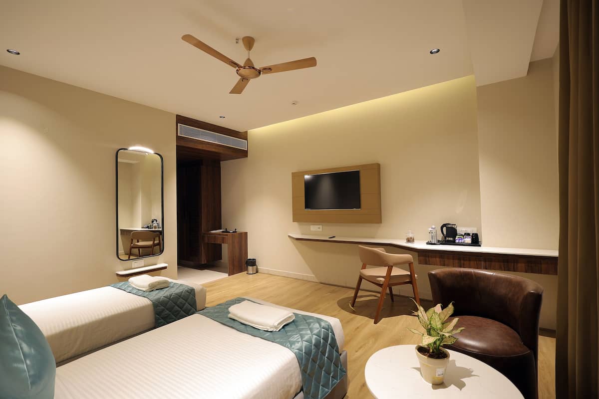 Habitación de hotel con dos camas, un escritorio, una silla, un televisor y un ventilador de techo.