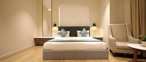 A modern hotel room with a large bed, a chair, a small table, and a mirror.