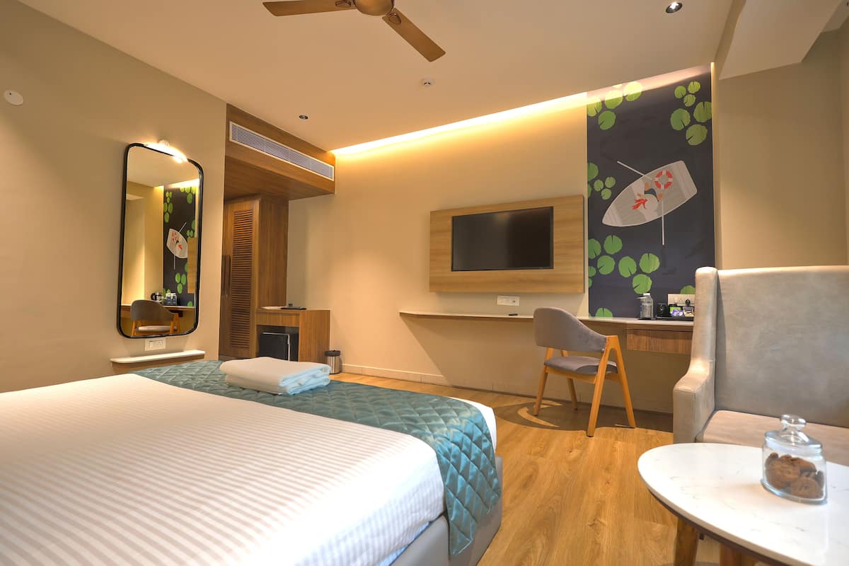 Habitación de hotel con cama, escritorio, silla, televisor y una pequeña mesa con un tarro de galletas.