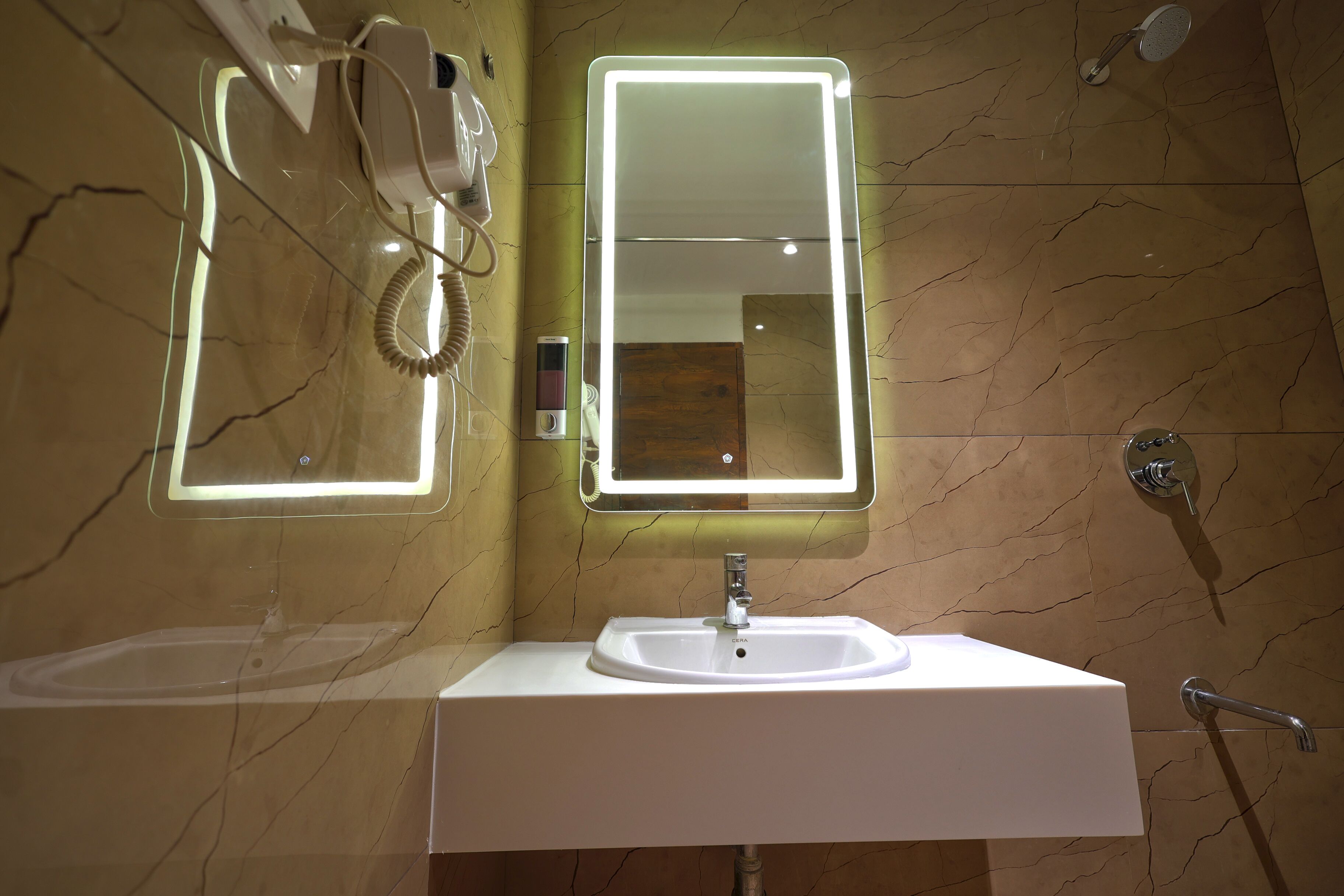 A bathroom with a white sink, a mirror with a light, a hairdryer, and a shower.