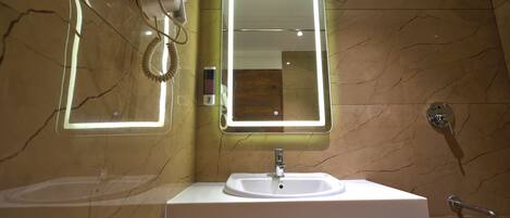 A bathroom with a white sink, a mirror with a light, a hairdryer, and a shower.