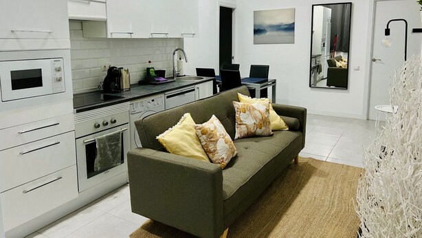 A modern kitchen with white cabinets, a built-in oven, and a dining area with a table and chairs. - Apartamento Huerta del Convento (Madrid)