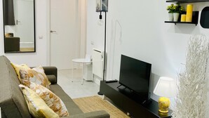 A modern living room with a sofa, a flat-screen TV, a small white side table, a mirror, and a shelf with decorative items. - Apartamento Huerta del Convento (Madrid)