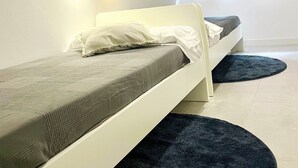 A single bed with a white frame and a grey mattress, a dark blue rug, and a white wall with two wall-mounted lights. - Apartamento Huerta del Convento (Madrid)