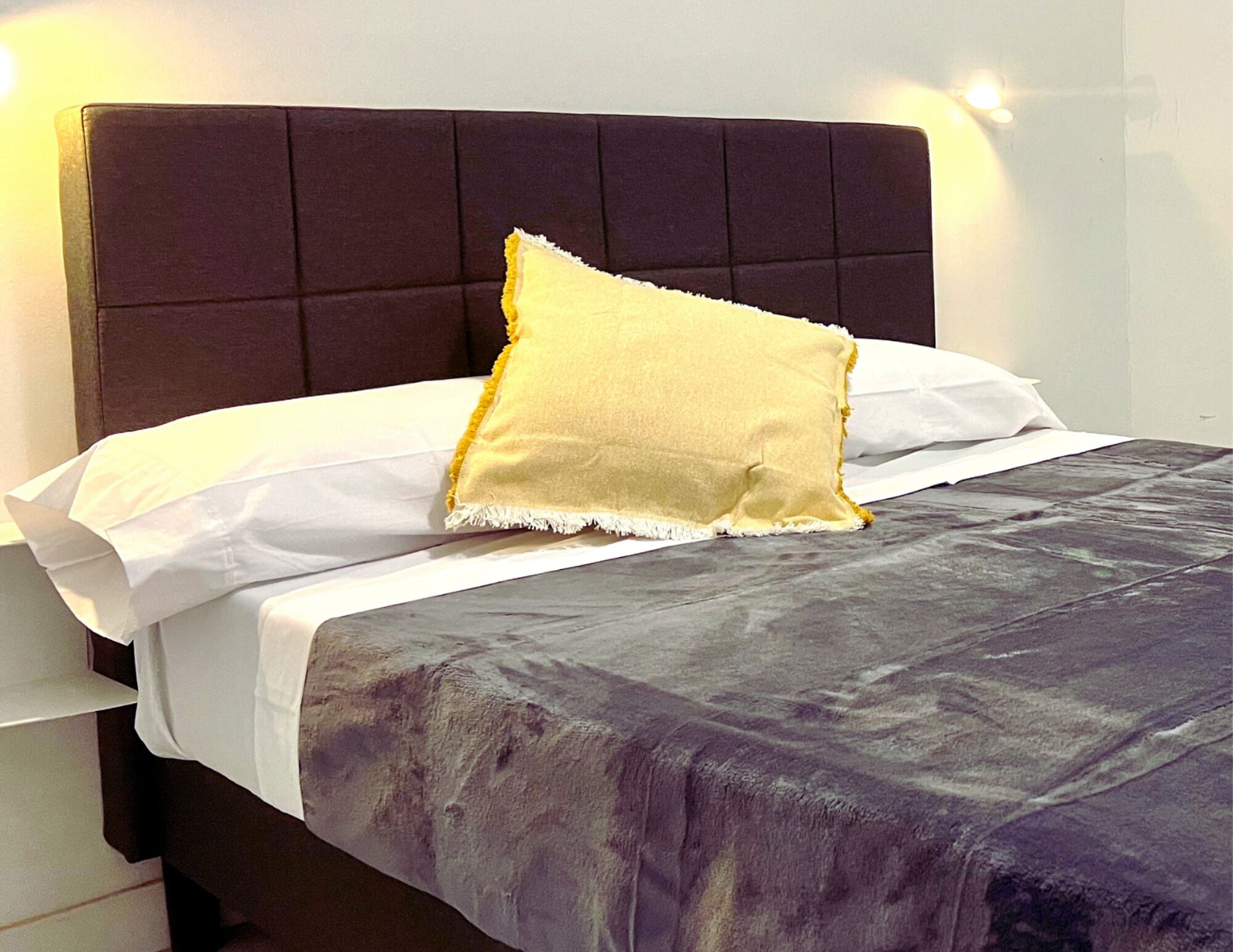 A bed with a dark headboard, white linens, and a yellow pillow.