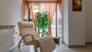 A room with a rocking chair, a radiator, a potted plant, and a window with curtains.