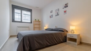 A bedroom with a bed, bedside tables, a radiator, a window, and wall decorations.