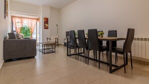 A dining area with a table and chairs, a sofa, a lamp, and a potted plant.