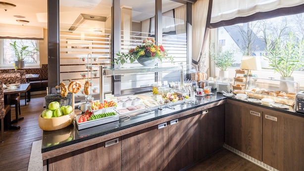 A buffet area with a variety of food items, a bowl of apples, and a flower arrangement. - Hotel Stadtidyll (Rotenburg)