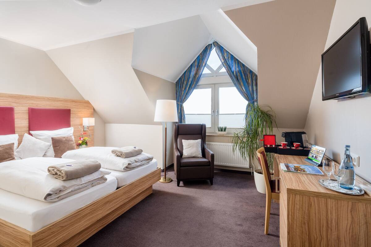 A hotel room with a bed, a desk, a chair, a TV, and a window with curtains.