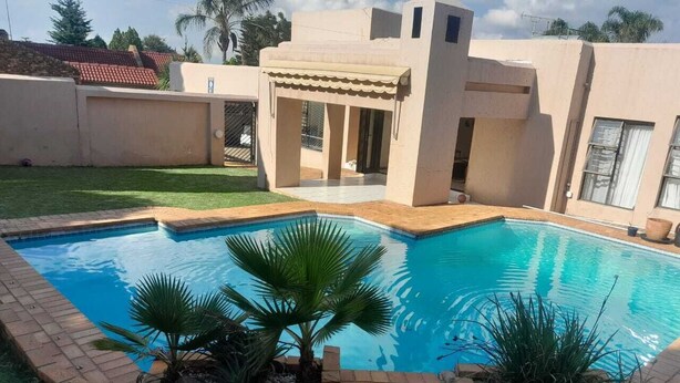 Una piscina con borde de baldosas, rodeada por un muro de ladrillo bajo y plantas de palma.