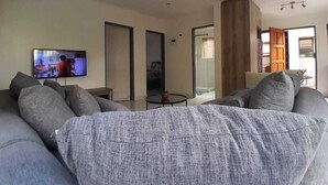 Un salón moderno con un sofá grande de color gris, un televisor de pantalla plana y un ventanal que da a un balcón.