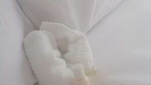 Un almohadón blanco con un cojín para el cuello blanco y una botella blanca sobre un sofá blanco.