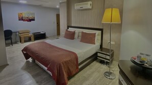 Une chambre d’hôtel moderne équipée d’un lit, d’une table de chevet, d’une lampe et d’un bureau avec une chaise.