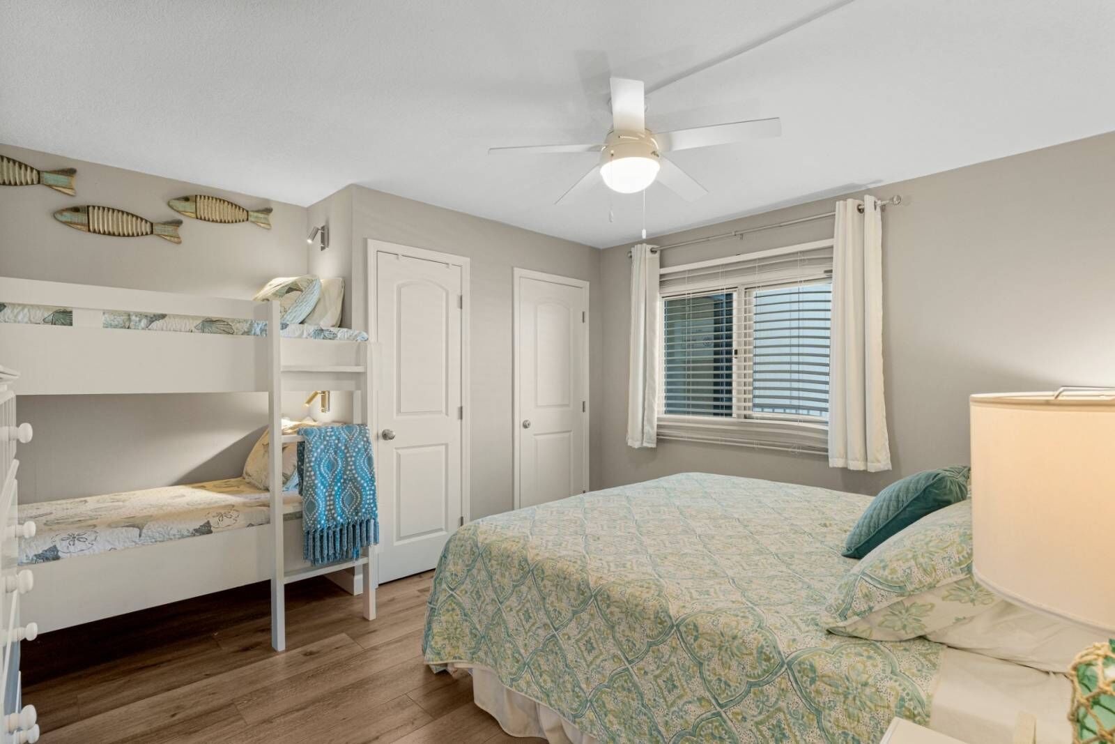 A bedroom with bunk beds, a ceiling fan, a window with blinds, and a bed with a patterned bedspread.