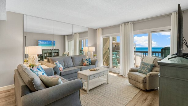 Een moderne woonkamer met een bank, salontafel en een televisie. Er is een balkon met uitzicht op de oceaan.