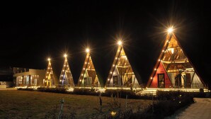 A row of triangular glass-roofed cabins with exterior lighting, connected by a pathway. - Sunflower Saga (Jamwa Ramgarh)