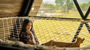 A hammock suspended between wooden beams in a room with large windows. - Sunflower Saga (Jamwa Ramgarh)