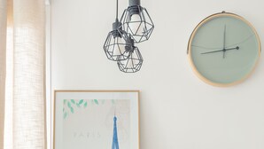 Een houten eettafel met een lijstwerk afbeelding van Parijs, een glazen kan, een pak zakdoekjes en een mand met snacks.