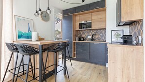 Een moderne keuken met houten kastjes, een ingebouwde oven en een koffieapparaat. Er staan twee zwarte barkrukken en een houten tafel.
