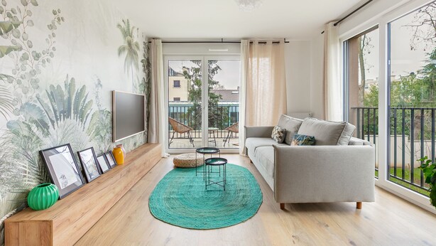 Een moderne woonkamer met een grijze bank, een blauwgroen vloerkleed en ingelijste foto's op een houten dressoir.