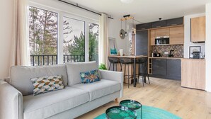 Een moderne woonkamer met een grijze bank, een eethoek met een zwarte tafel en een keuken met houten kasten en een zwart aanrecht.