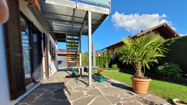 Un patio empedrado con una mesa y sillas, un regador verde, una planta en maceta y una valla de madera.