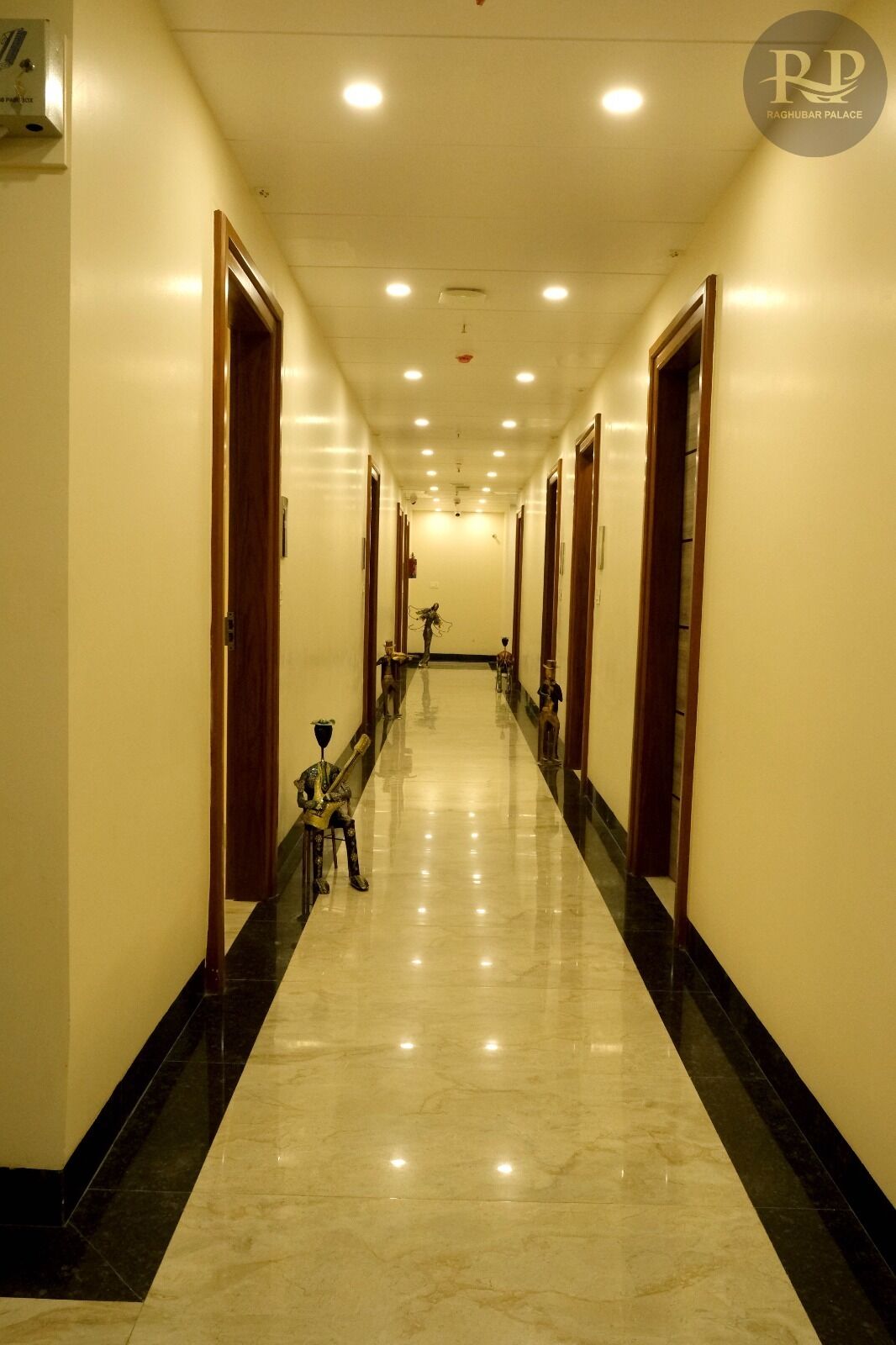 A hotel corridor with a marble floor, wooden doors, and a sign for Raghubar Palace.