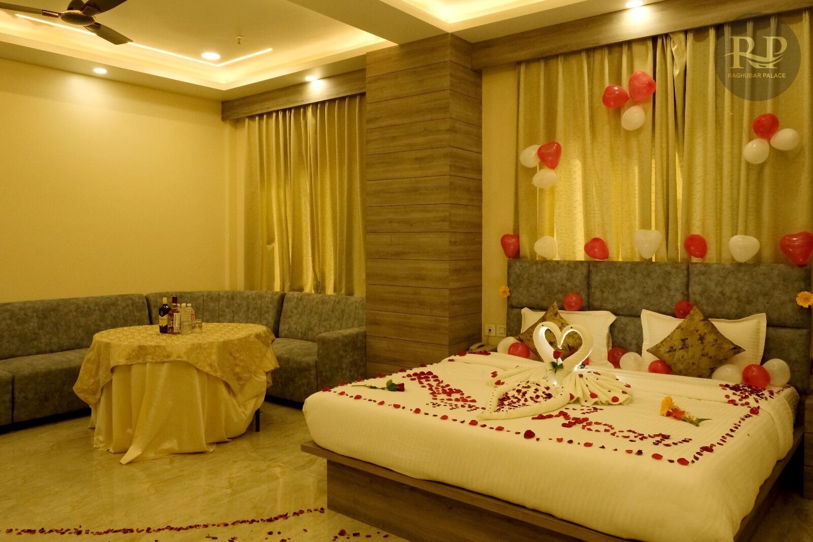 A hotel room with a large bed, a sofa, a small table with drinks, and a ceiling fan.