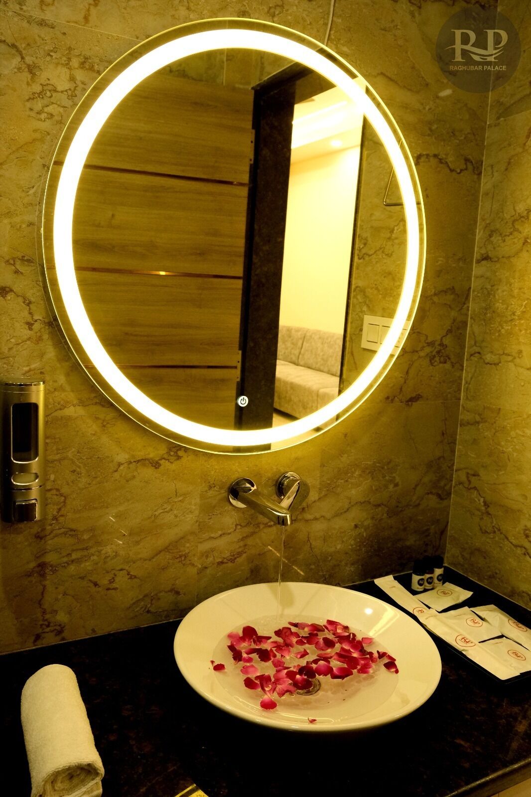 A bathroom with a round mirror, a sink with rose petals, and a towel on the counter.