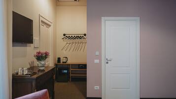 Una habitación de hotel con cama, escritorio con un florero, perchero y microondas.