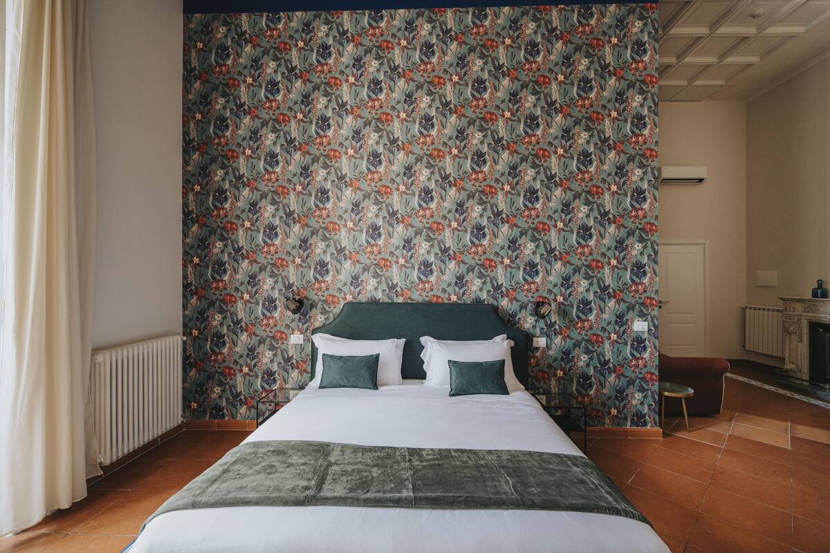 Ein Schlafzimmer mit Blumenwallpaper, einem Bett mit grüner Bettwäsche und einem Heizkörper.