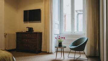 A room with a wooden dresser, a television mounted on the wall, a chair, and a window with curtains.