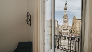 A balcony with a wrought iron railing, a view of a historic building with a statue, and a chair in the foreground. - Palazzo Pandola - Luxury Suites (Naples)