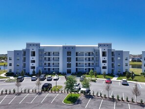 A multi-story parking garage with several cars parked, surrounded by a landscaped area with small trees and a clear blue sky. - Fun 2BR Retreat! Theme Room, Lake View near Disney (Kissimmee)