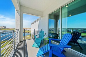 A balcony with a view of a body of water and buildings, furnished with blue chairs and a table.