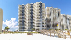A beachfront high-rise hotel with multiple balconies, a wooden boardwalk, and a sandy beach.